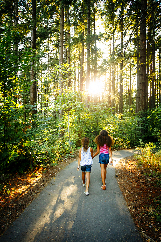 Mixed Race sisters holding hands walking on forest path