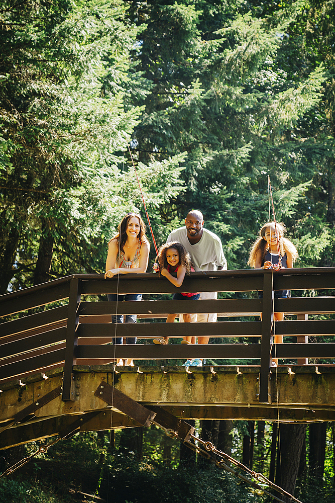 Multi-ethnic family fishing on bridge over river