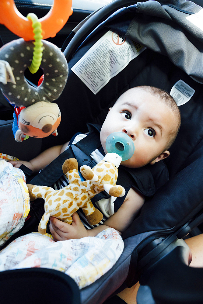 Curious Mixed Race baby boy with pacifier in car seat