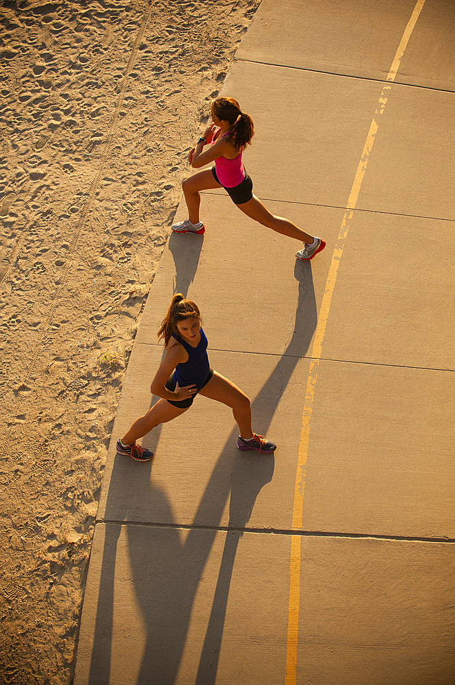 Mixed Race mother and daughter stretching on path at beach