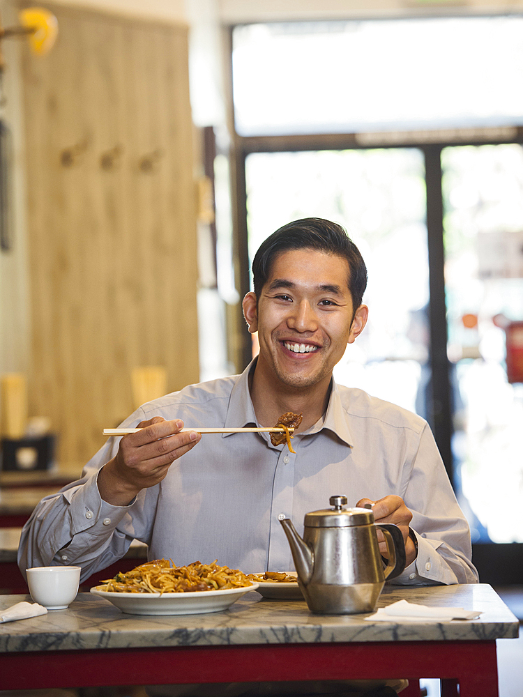 Chinese man eating with chopsticks in restaurant