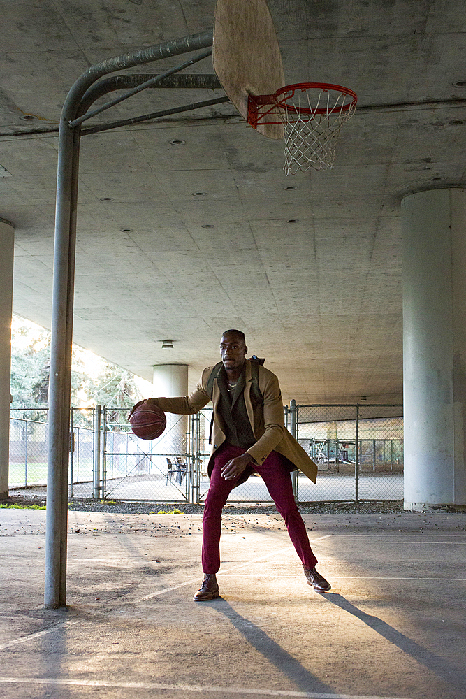 Black man wearing backpack playing basketball under overpass