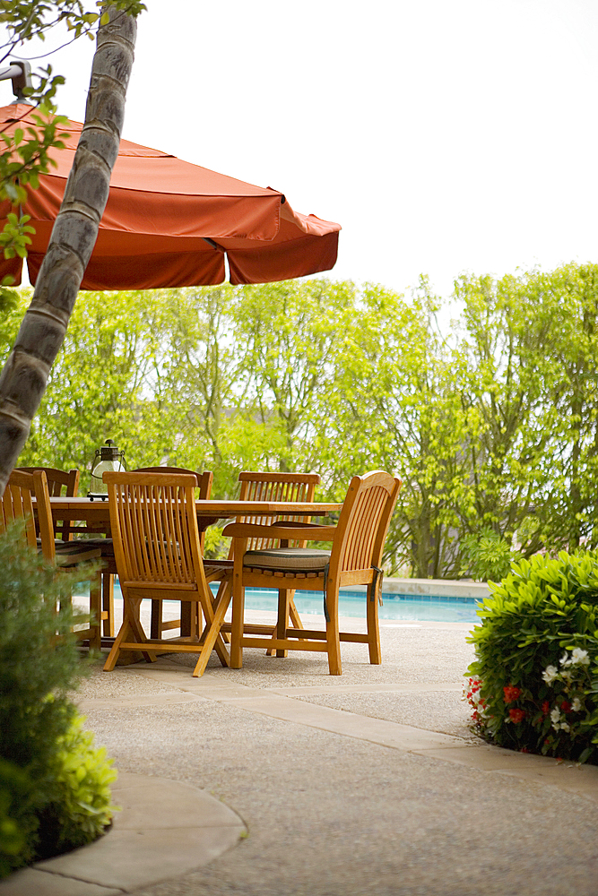 Detail of sitting area by pool covered with red umbrella.