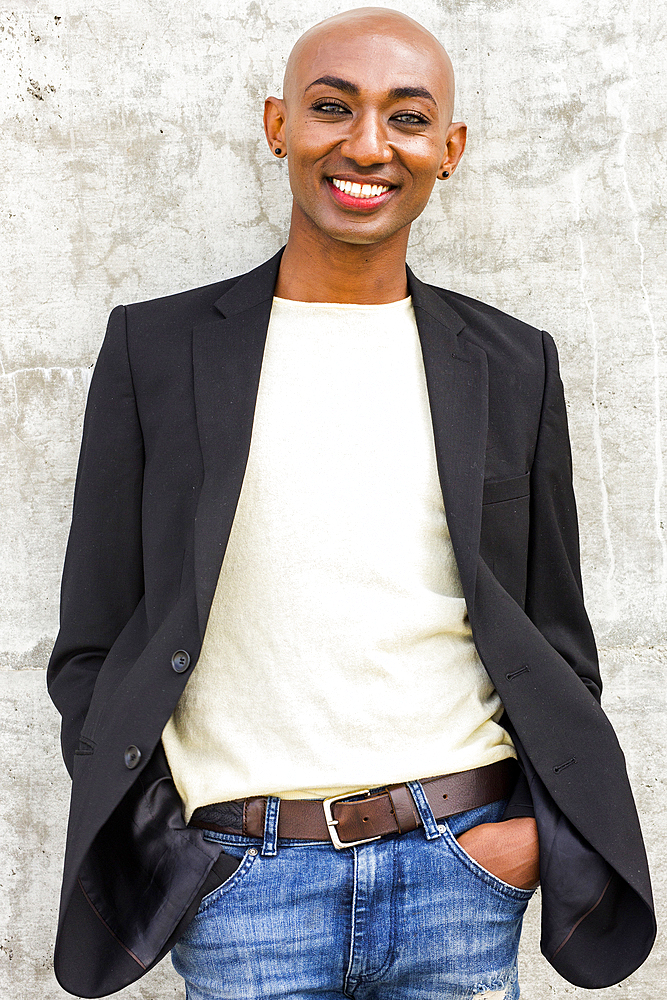 Smiling gay Black man leaning on concrete wall