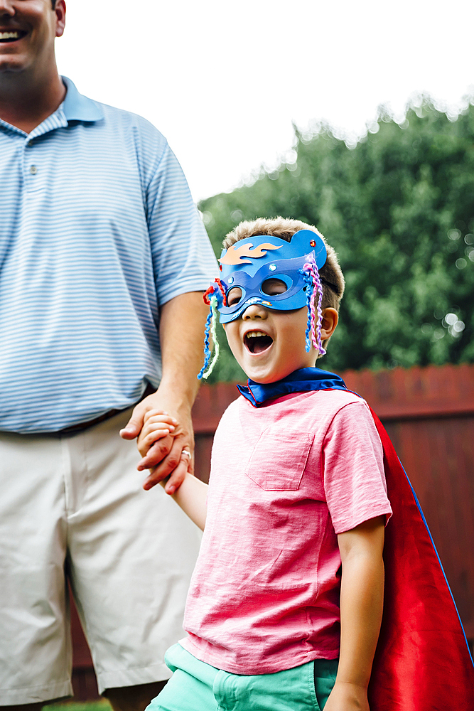 Caucasian father and superhero son holding hands