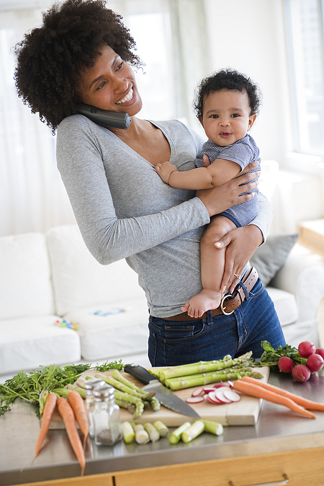 Mother talking on telephone while holding baby son in kitchen