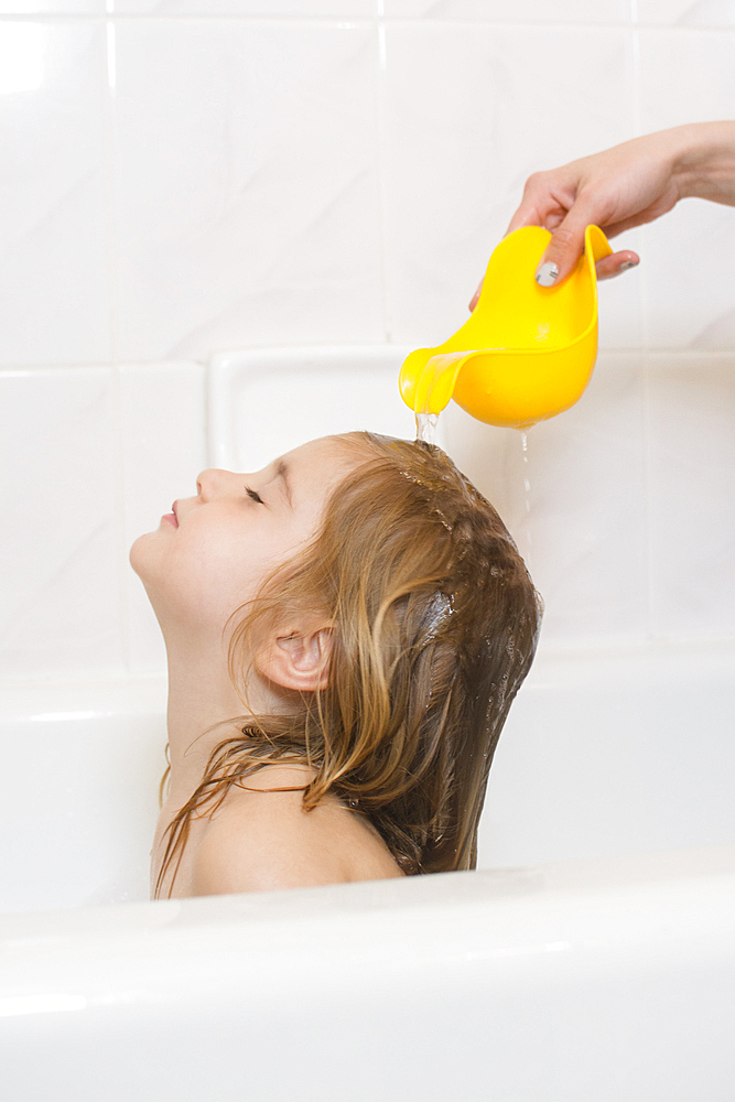 Caucasian mother rinsing hair of daughter in bathtub