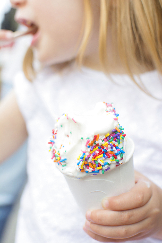 Caucasian girl eating cup of ice cream with sprinkles