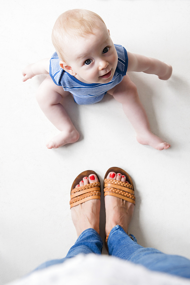 Caucasian baby boy sitting on floor at feet of mother