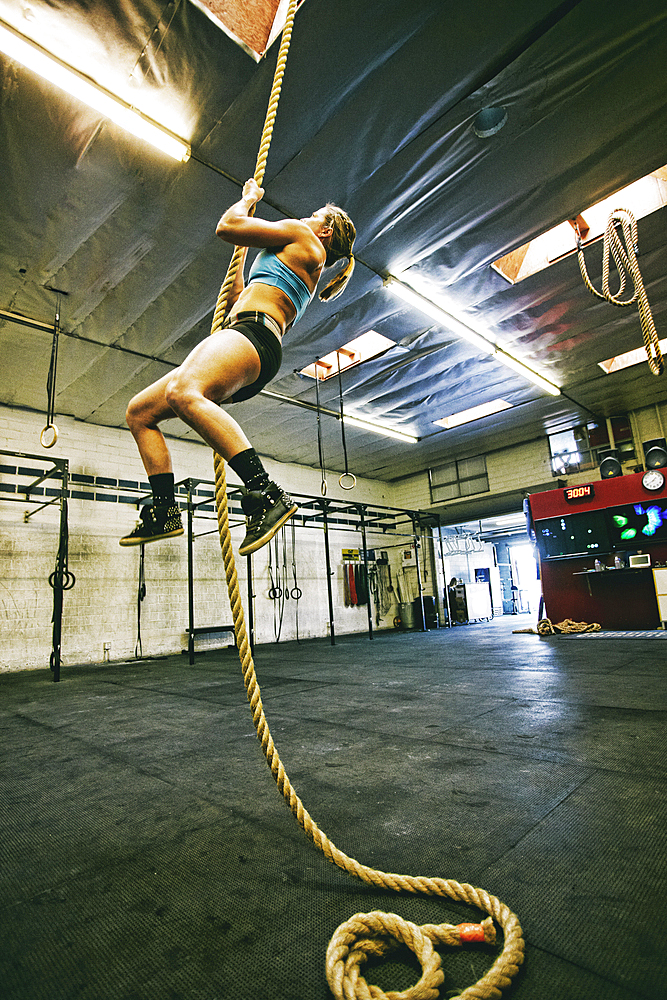 Caucasian woman climbing rope in gymnasium