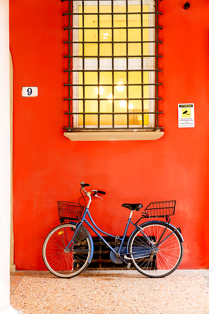 Blue bicycle leaning on orange wall under window