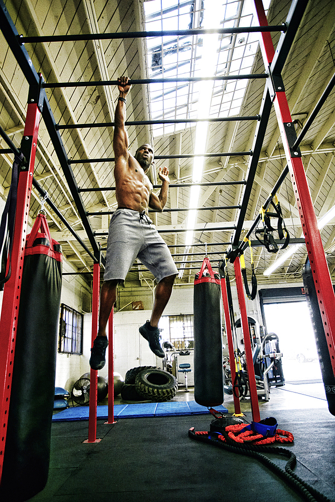 Black man hanging from bars in gymnasium