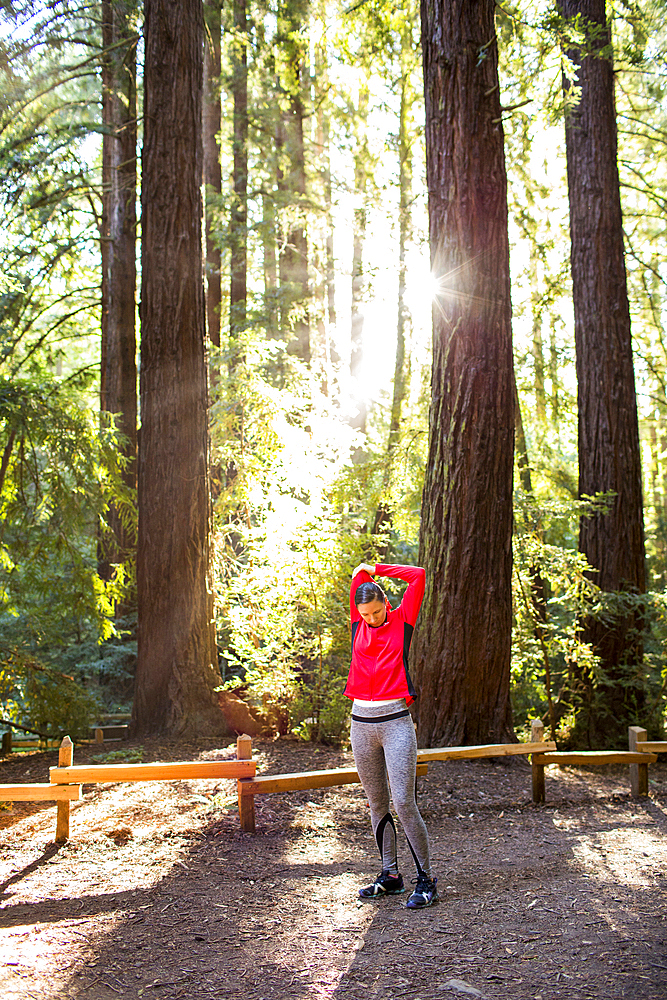 Serious woman stretching arm on forest path