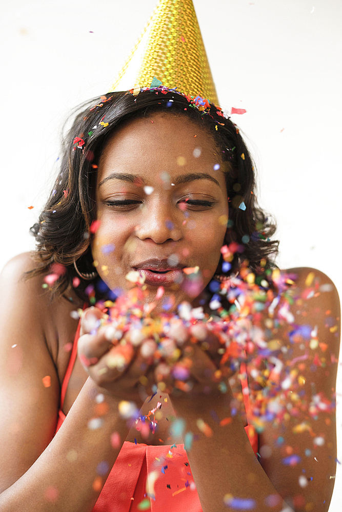 Mixed Race woman wearing party hat blowing confetti