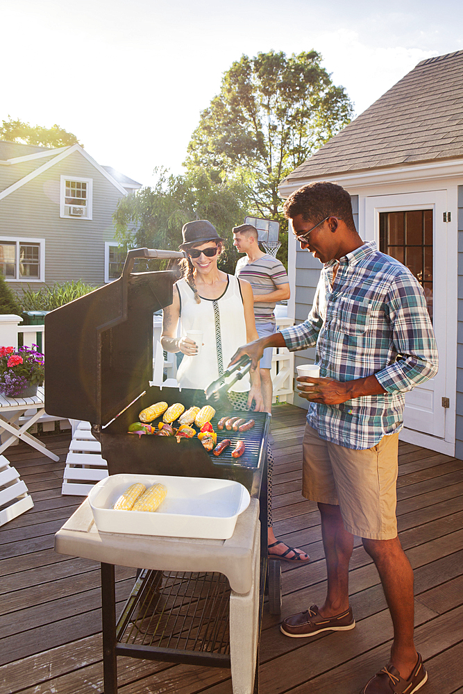 Friends cooking food on grille at barbecue on patio