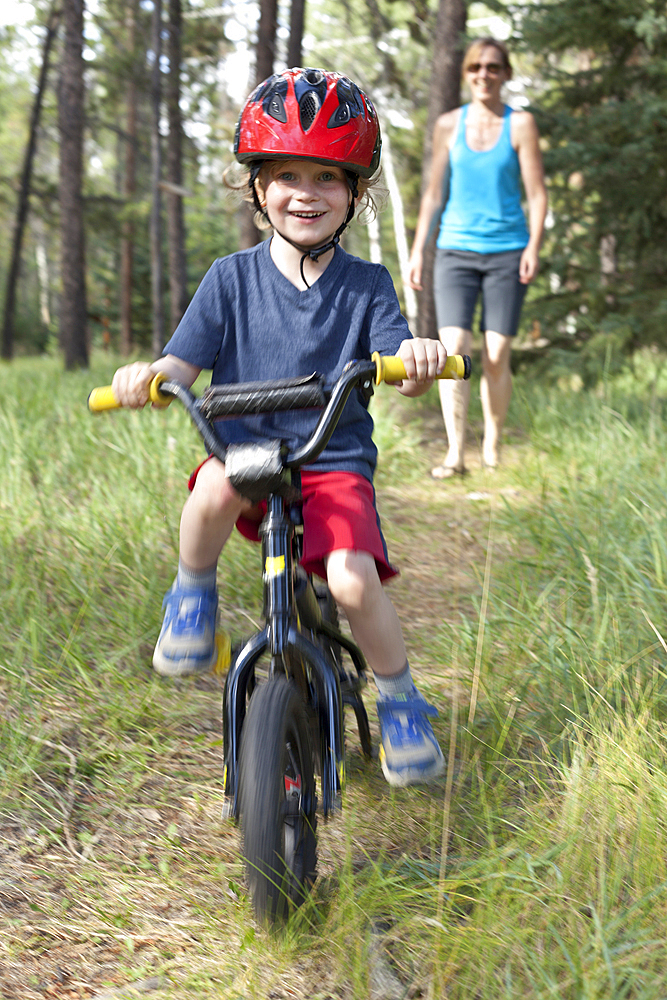 Caucasian mother watching smiling son on bicycle