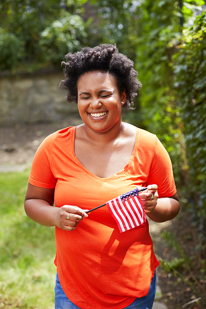 Portrait of laughing Black woman holding little American flag