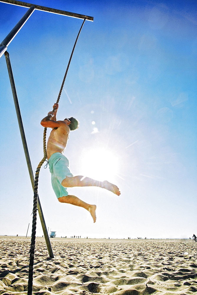 Caucasian man climbing rope on beach