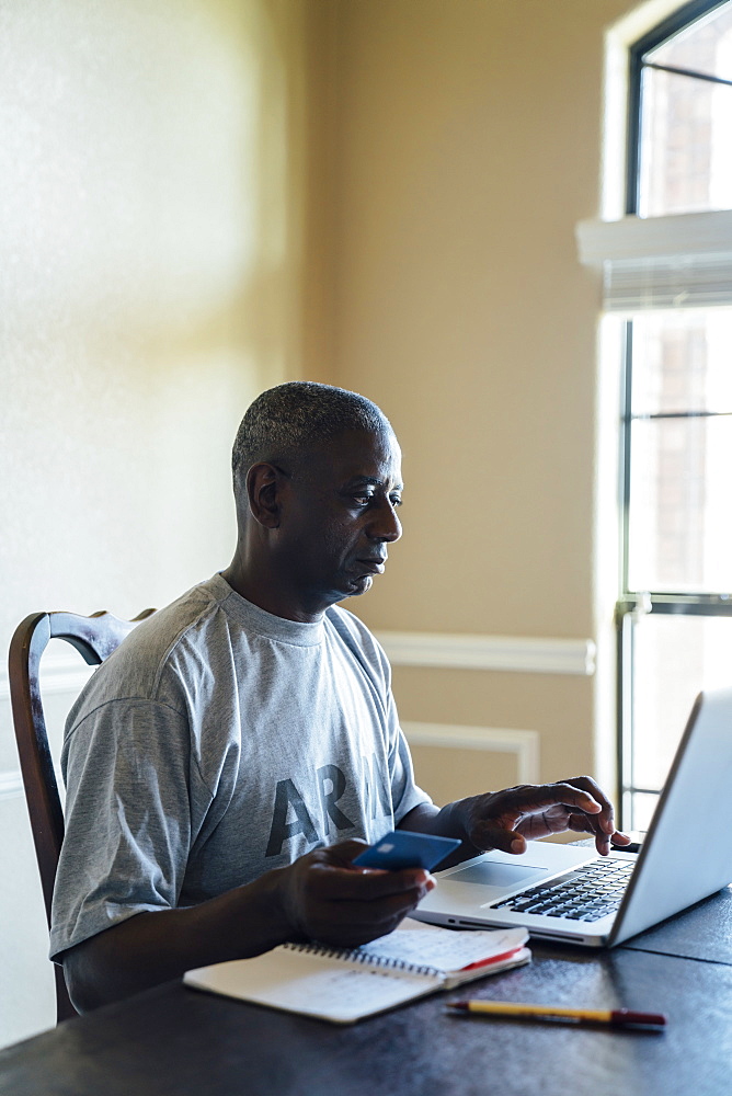 Black man using credit card with laptop at table