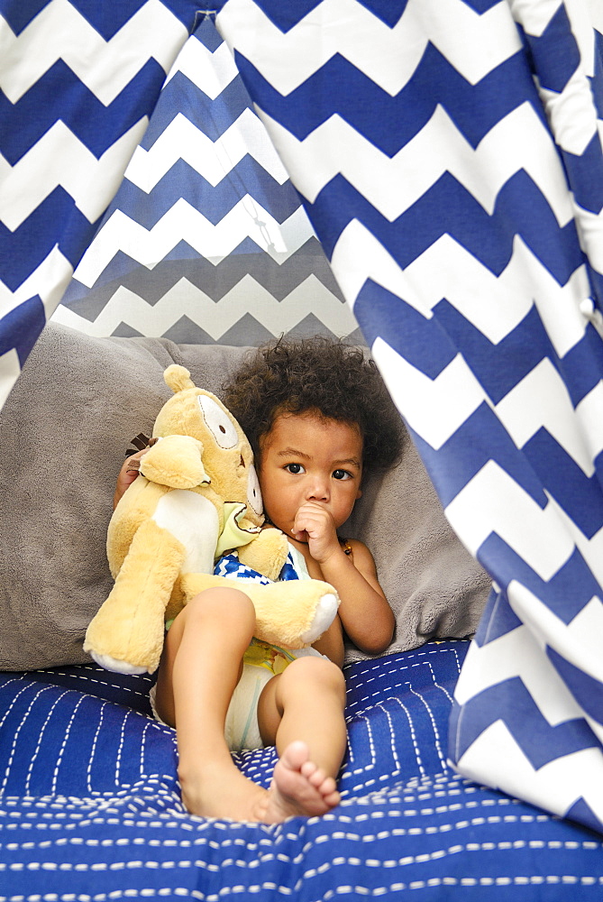 Mixed Race baby boy sucking thumb holding stuffed animal