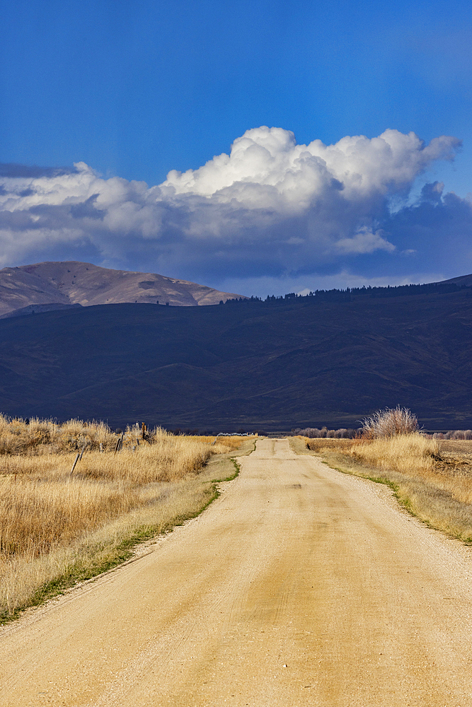 Empty dirt road leading to foothills under stormy skies