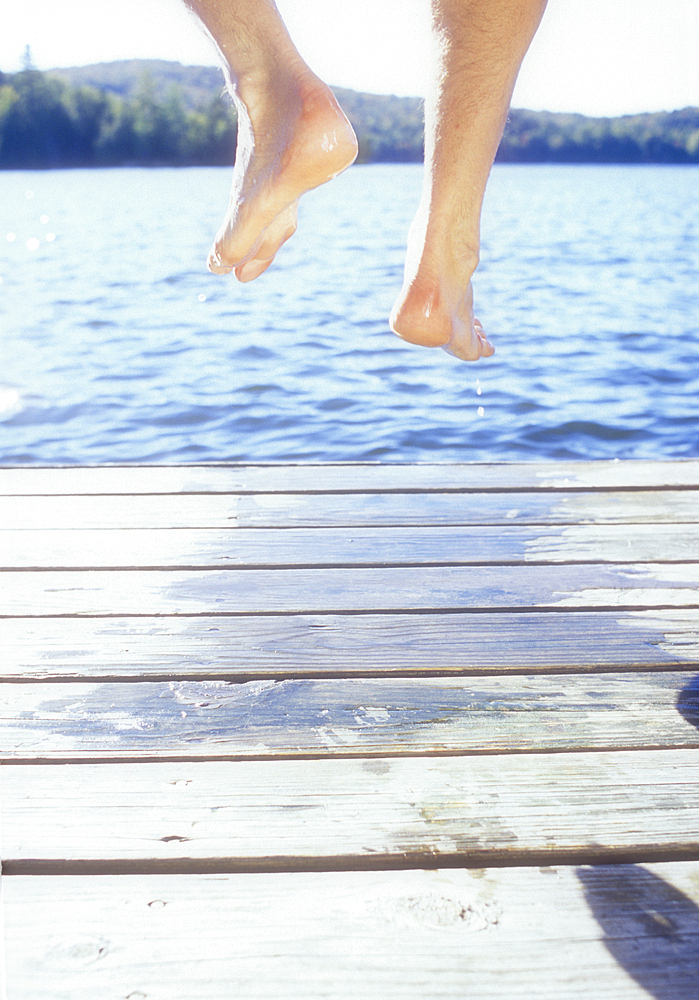 Legs of man jumping off dock into lake, Saranac Lake, New York, USA