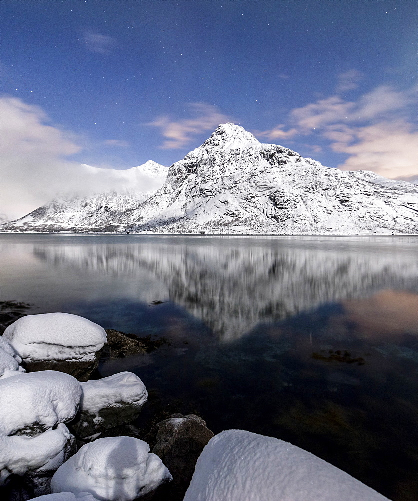 The snowy peaks are reflected in the cold sea under a starry sky, Vareid, Flakstad, Nordland, Lofoten Islands, Northern Norway, Scandinavia, Europe