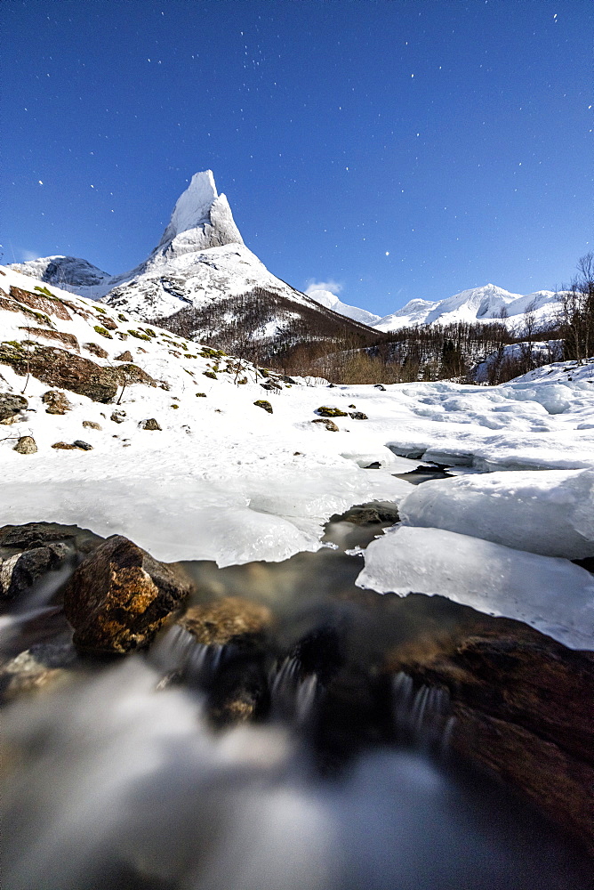 Ice on rocks frames the granitic snowy peak of the Stetind mountain under the starry sky, Tysfjord, Nordland, Norway, Scandinavia, Europe