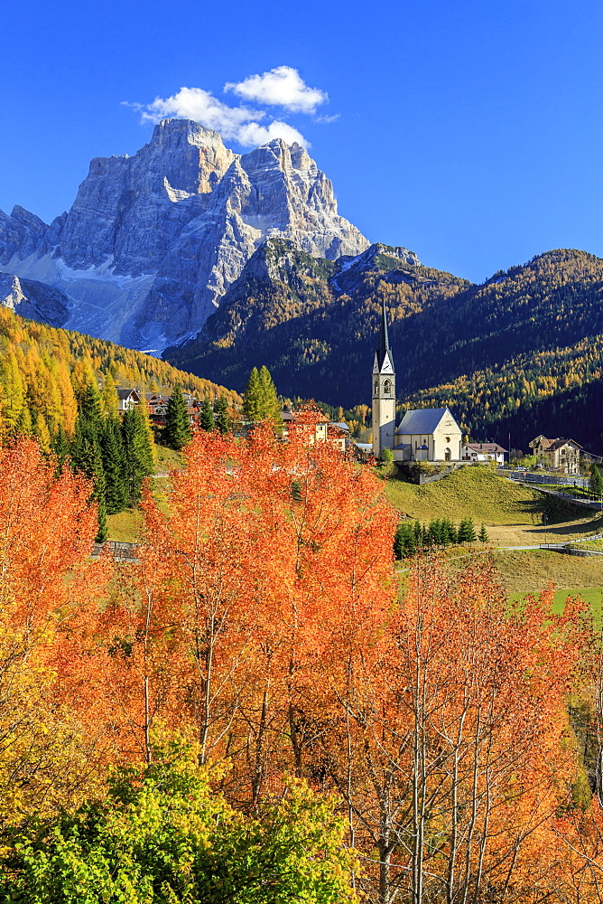 Red and orange trees in front of the tiny church of Selva di Cadore, in the Dolomites, with Mount Pelmo in the background, Veneto, Italy, Europe