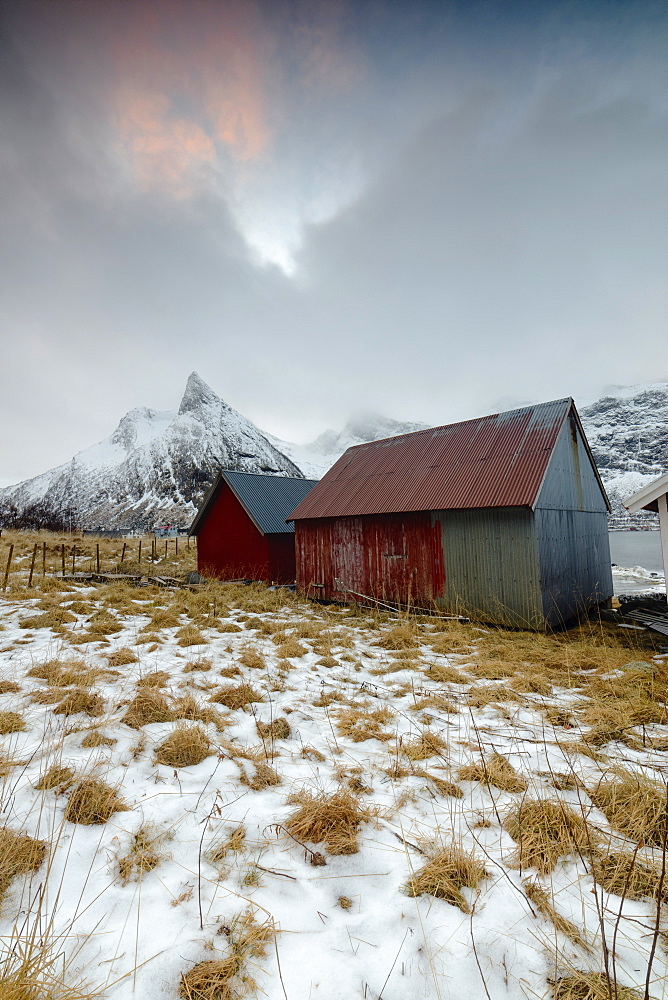 Clouds on snowy peaks above typical wooden hut called Rorbu, Senja, Ersfjord, Troms county, Norway, Scandinavia, Europe