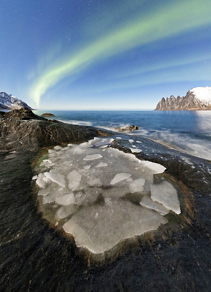 The Northern Lights (aurora borealis) illuminate the rocky peaks and icy sea in the polar night, Tungeneset, Senja Troms, Norway, Scandinavia, Europe