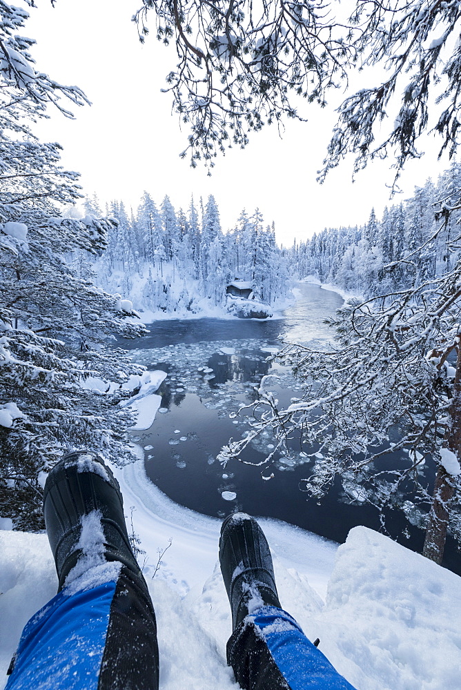 Hiker rests on the snow above Myllykoski rapids, Juuma, Oulanka National Park, Kuusamo, Lapland, Finland, Europe