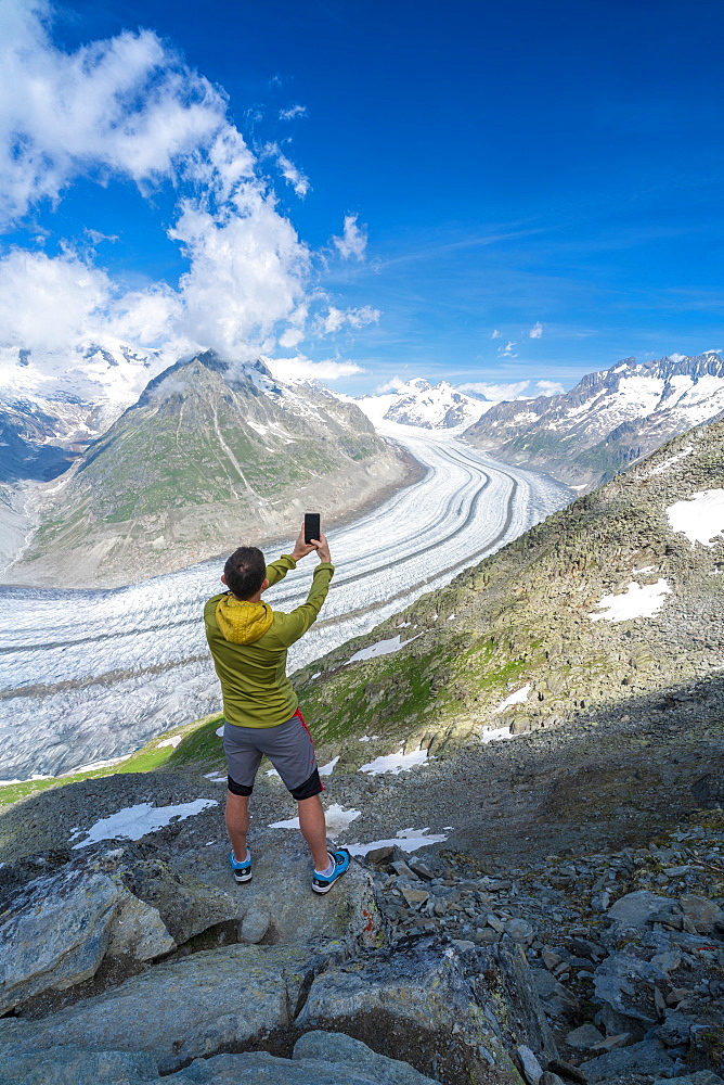 Rear view of man photographing Aletsch Glacier with smartphone from Eggishorn viewpoint, Bernese Alps, canton Valais, Switzerland, Europe