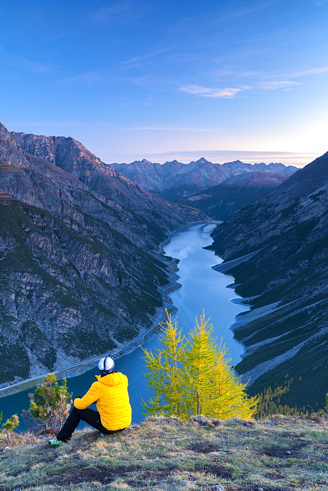 Hiker admiring lake and mountains at dawn sitting on Crap de La Pare, Livigno, Sondrio province, Valtellina, Lombardy, Italy, Europe