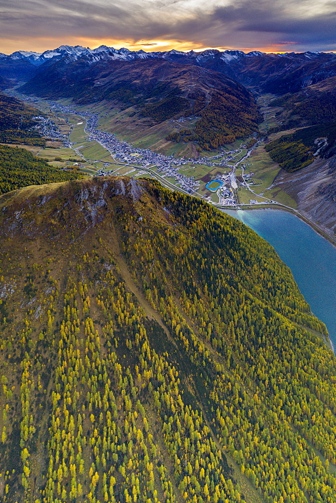 Sunset over larch woods on Crap de La Pare ridge towards Livigno village and lake, aerial view, Valtellina, Lombardy, Italy, Europe