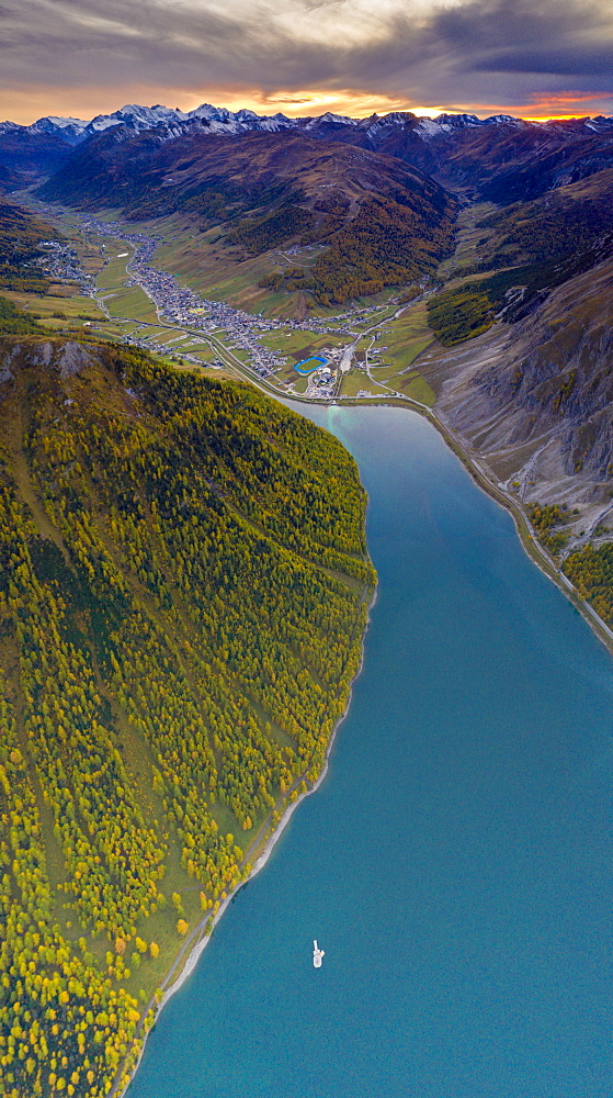 Aerial panoramic of sunset over Livigno and larch trees along the lake in autumn, Sondrio province, Valtellina, Lombardy, Italy, Europe