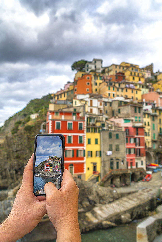 Personal perspective of man photographing Riomaggiore with smartphone, Cinque Terre, UNESCO World Heritage Site, La Spezia province, Liguria, Italy, Europe