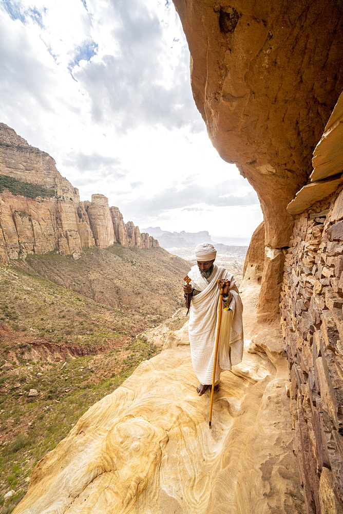 Priest holding the hand cross on rocks outside Abuna Yemata Guh church, Gheralta Mountains, Tigray Region, Ethiopia, Africa