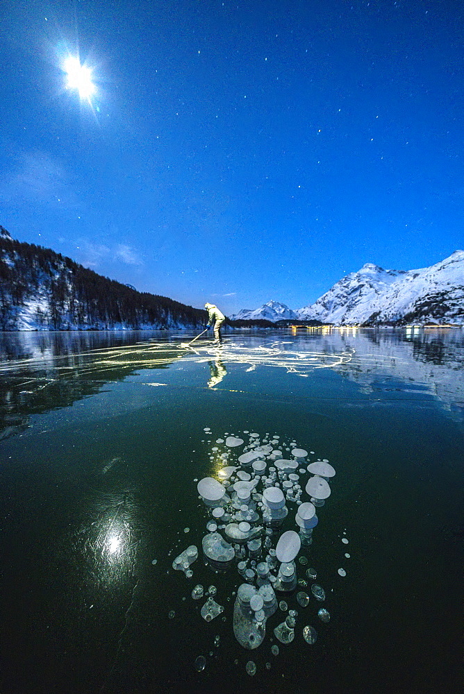 Full moon on ice skater on frozen Lake Sils lit by head torch, Engadine, canton of Graubunden, Switzerland, Europe