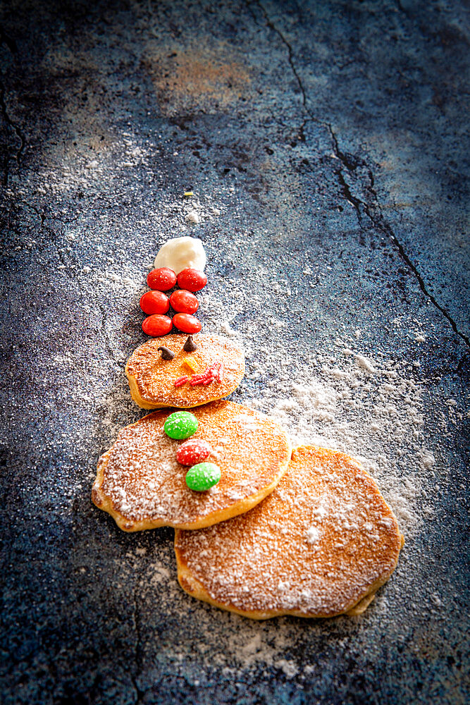 Home made pancakes in shape of snowman decorated with sugar buttons on table background at Christmas time, Italy, Europe