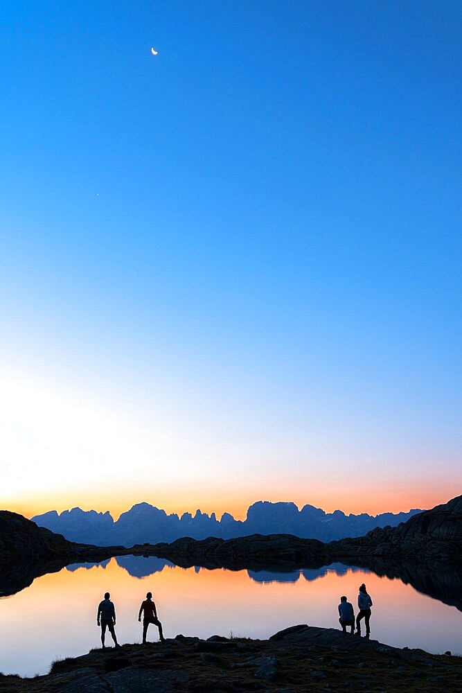 Hikers admiring Brenta Group Dolomites reflected in Lago Nero di Cornisello at dawn, Trento,Trentino-Alto Adige, Italy, Europe