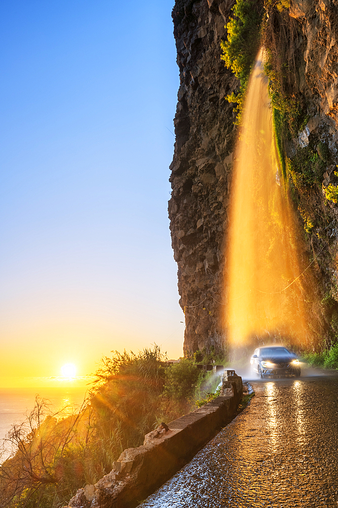 Car passing under Anjos waterfall on slippery coastal road at sunset, Ponta do Sol, Madeira island, Portugal, Atlantic, Europe