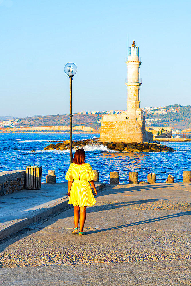 Charming woman with dress walking to the old lighthouse at sunset, Chania, Greek Islands, Greece, Europe