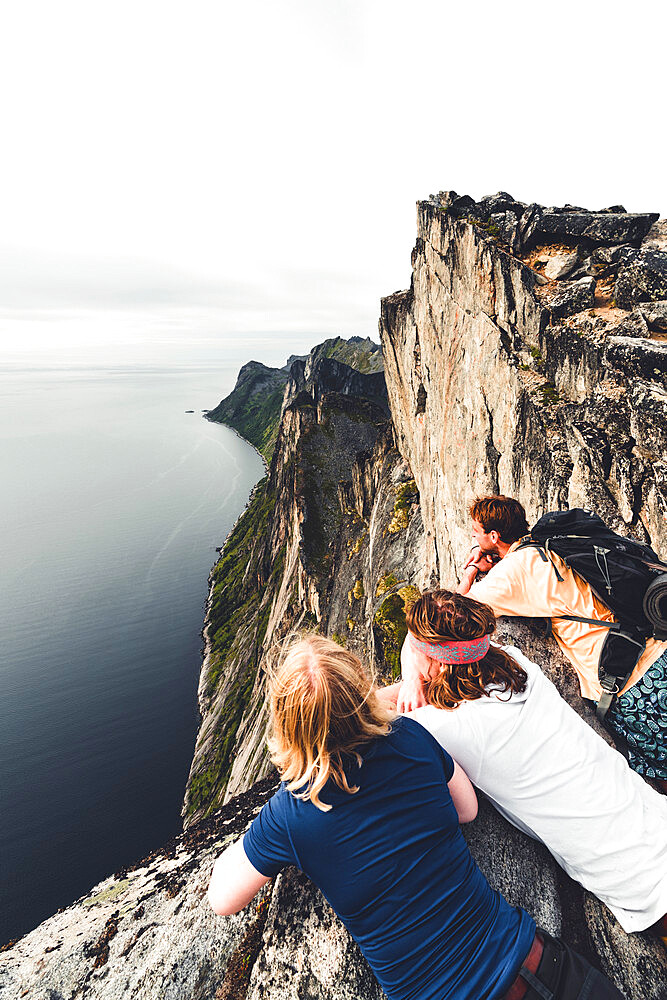 Three friends enjoying the view of the fjord leaning on rocks on Segla mountain peak, Senja island, Troms county, Norway, Scandinavia, Europe