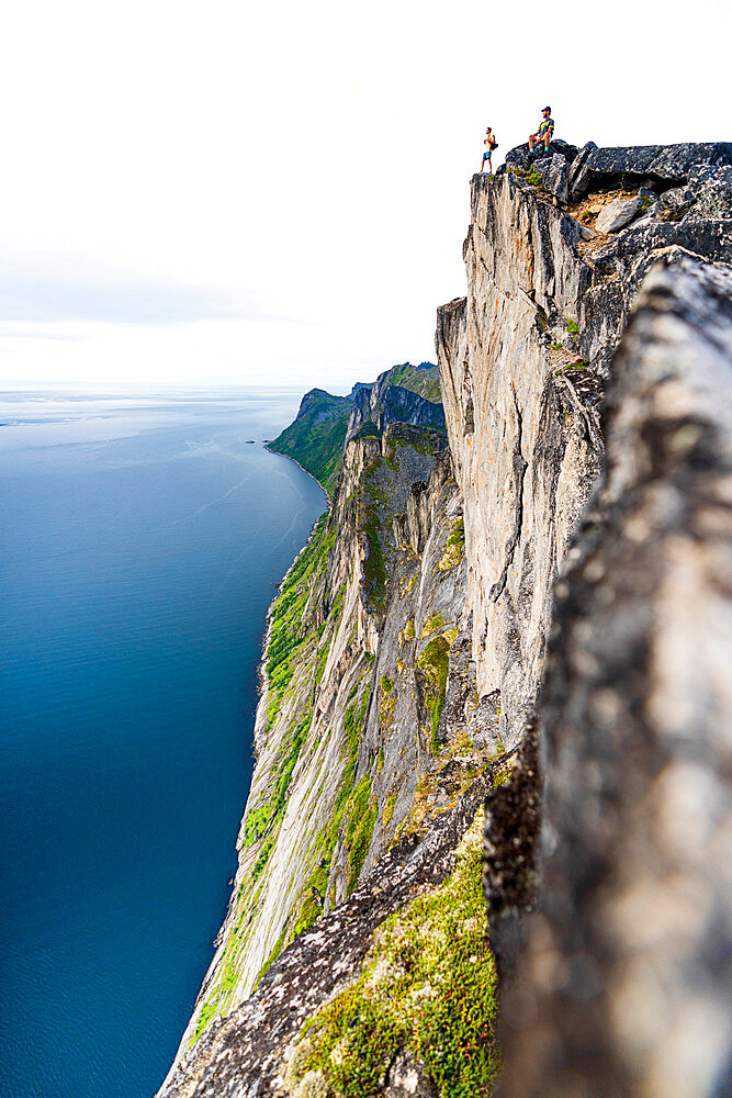 Two people watching the blue water of the fjord standing on rocky peak of Segla mountain, Senja, Troms county, Norway, Scandinavia, Europe