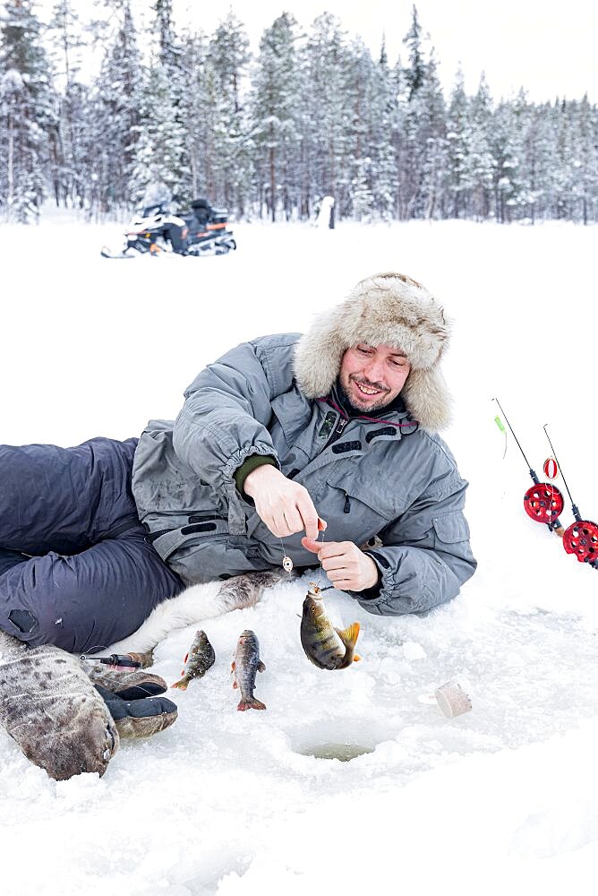 Cheerful man picking up the catch of fish from ice hole, Lapland, Sweden