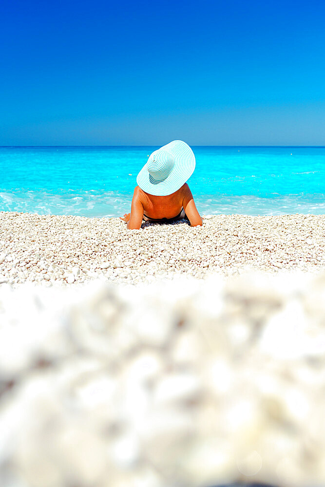 Woman with straw hat contemplating the sea lying on a beach in summer, Kefalonia, Ionian Islands, Greek Islands, Greece, Europe