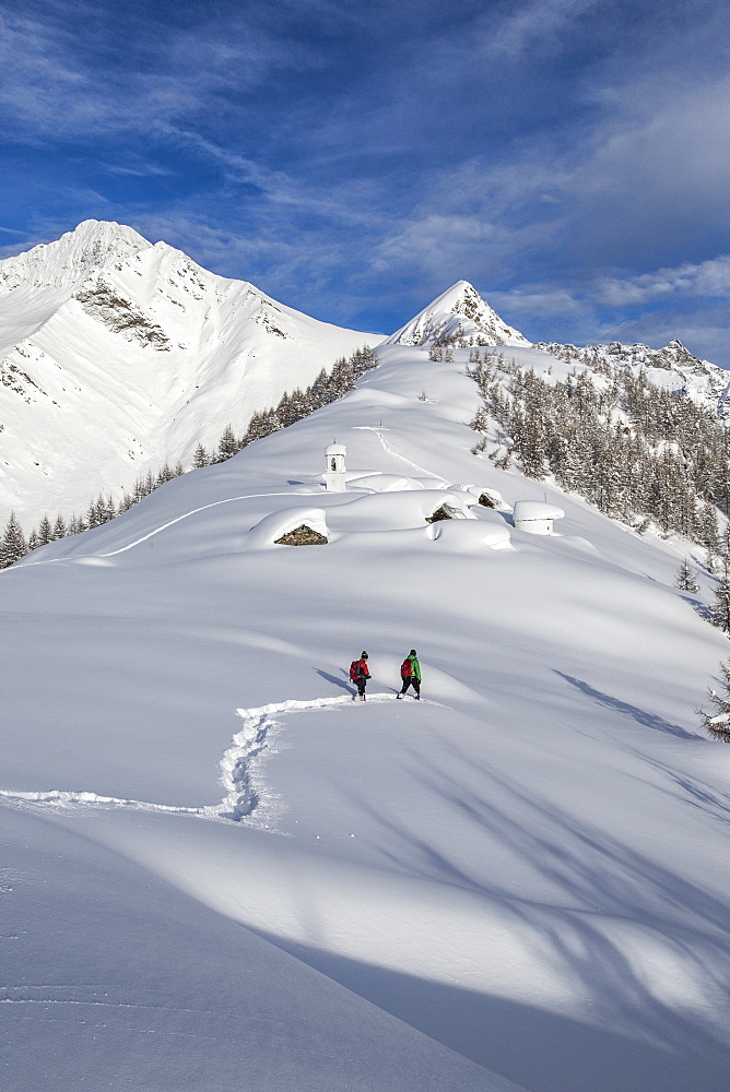 Hikers trying to approach the little village at the Scima Alp covered in snow, Valchiavenna, Lombardy, Italy, Europe