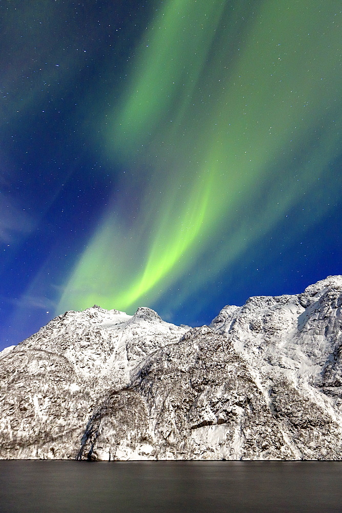 Northern Lights (aurora borealis) illuminate the snowy peaks and the blue sky during a starry night, Budalen, Svolvaer, Lofoten Islands, Arctic, Norway, Scandinavia, Europe