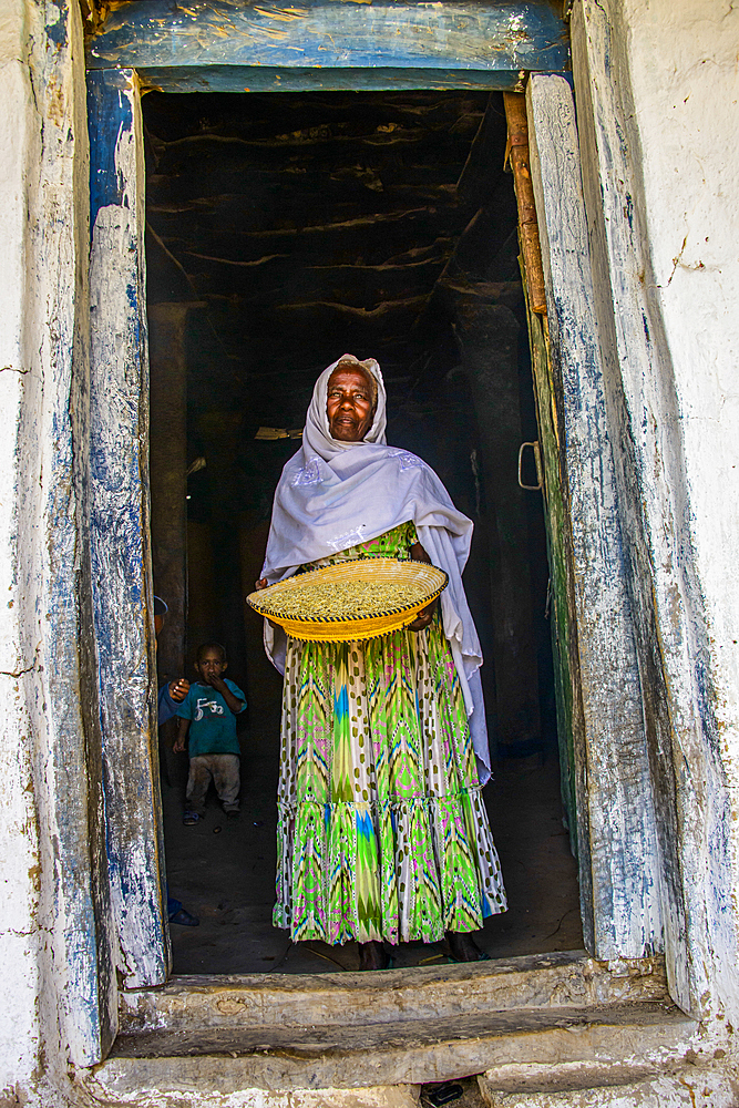 Friendly old woman standing with a basket of corn in a door frame, near Keren, Eritrea, Africa